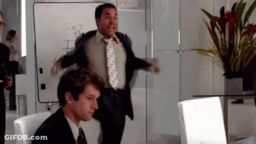 A Man In A Suit And Tie Is Jumping In The Air In Front Of A White Board That Says Get GIF