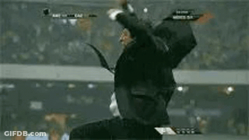 A Man In A Suit And Tie Is Jumping In The Air While Watching A Soccer Game . GIF
