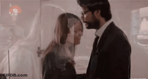 A Man In A Suit And Tie Is Kissing A Woman Behind A Glass . GIF