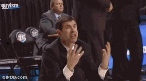 A Man In A Suit And Tie Is Kneeling On The Floor During A Basketball Game GIF