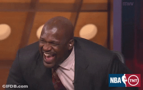 A Man In A Suit And Tie Is Laughing In Front Of An Nba Logo GIF