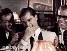 A Man In A Suit And Tie Is Laughing While Sitting At A Table In A Restaurant . GIF