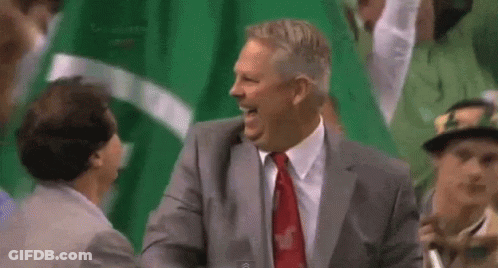 A Man In A Suit And Tie Is Laughing While Sitting In A Crowd . GIF