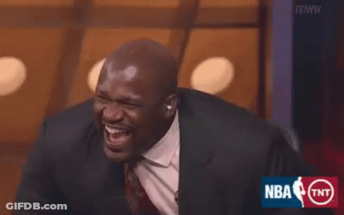A Man In A Suit And Tie Is Laughing While Sitting On A Stage . GIF