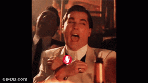 A Man In A Suit And Tie Is Laughing With A Red S On His Shirt GIF