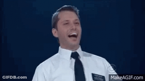 A Man In A Suit And Tie Is Laughing With His Mouth Open . GIF