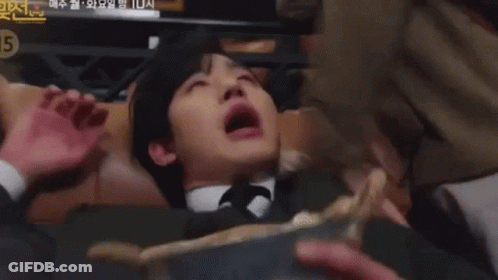 A Man In A Suit And Tie Is Laying On His Back With His Mouth Open . GIF