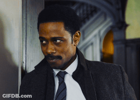 A Man In A Suit And Tie Is Leaning Against A Door GIF