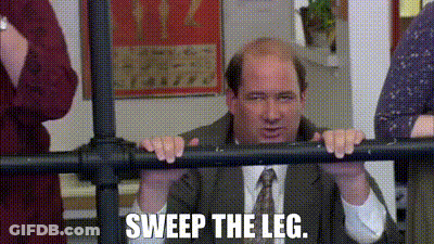 A Man In A Suit And Tie Is Leaning Against A Railing And Saying `` Sweep The Leg . '' GIF