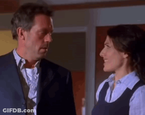 A Man In A Suit And Tie Is Looking At A Woman In A Blue Shirt . GIF
