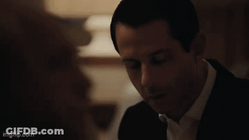 A Man In A Suit And Tie Is Looking At A Woman In A Room . GIF