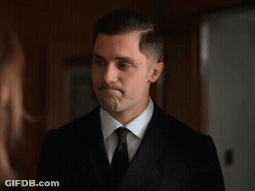 A Man In A Suit And Tie Is Looking At A Woman . GIF