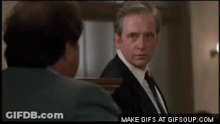 A Man In A Suit And Tie Is Looking At Another Man In A Suit And Tie . GIF
