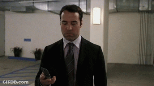 A Man In A Suit And Tie Is Looking At His Cell Phone . GIF