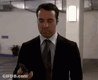 A Man In A Suit And Tie Is Looking At His Cell Phone . GIF