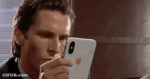 A Man In A Suit And Tie Is Looking At His Iphone . GIF
