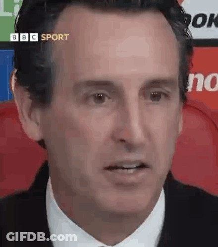 A Man In A Suit And Tie Is Looking At The Camera While Sitting In A Chair . GIF