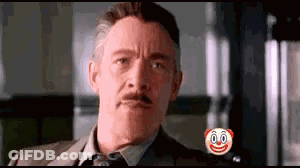 A Man In A Suit And Tie Is Looking At The Camera With A Clown Face On His Chest . GIF