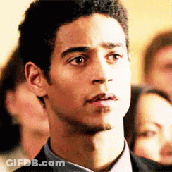 A Man In A Suit And Tie Is Looking At The Camera With A Group Of People In The Background . GIF