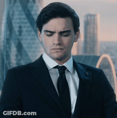 A Man In A Suit And Tie Is Looking Down With A City In The Background GIF