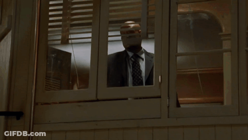 A Man In A Suit And Tie Is Looking Out A Window GIF