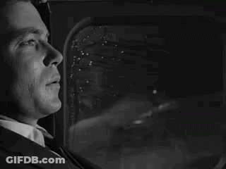 A Man In A Suit And Tie Is Looking Out Of A Window . GIF