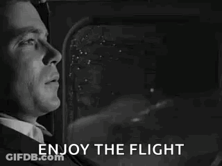 A Man In A Suit And Tie Is Looking Out The Window Of An Airplane And Saying `` Enjoy The Flight '' . GIF