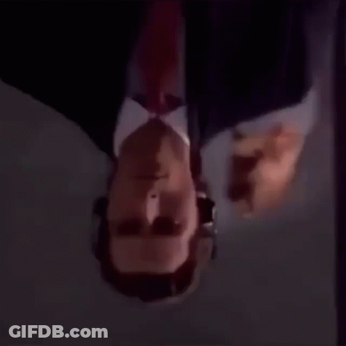A Man In A Suit And Tie Is Looking Upside Down . GIF