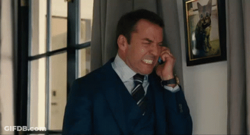 A Man In A Suit And Tie Is Making A Face While Talking On A Cell Phone GIF