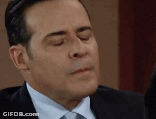A Man In A Suit And Tie Is Making A Face With His Eyes Closed . GIF
