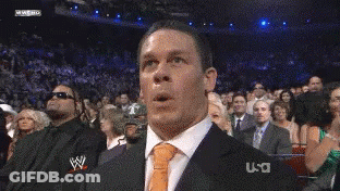 A Man In A Suit And Tie Is Making A Funny Face In Front Of A Crowd That Is Watching A Wrestling Match GIF