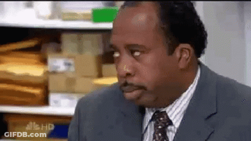 A Man In A Suit And Tie Is Making A Funny Face In Front Of A Shelf Of Envelopes . GIF