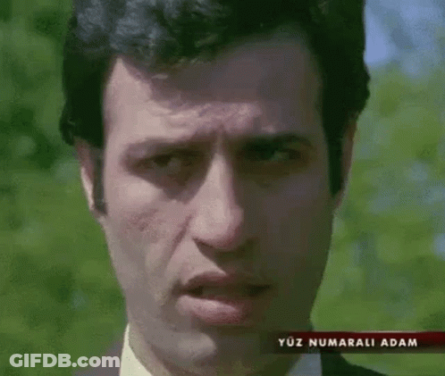 A Man In A Suit And Tie Is Making A Funny Face In Front Of Trees . GIF
