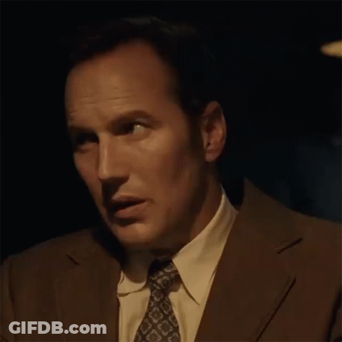 A Man In A Suit And Tie Is Making A Funny Face In The Dark . GIF