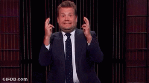 A Man In A Suit And Tie Is Making A Funny Face While Holding His Fingers Crossed . GIF