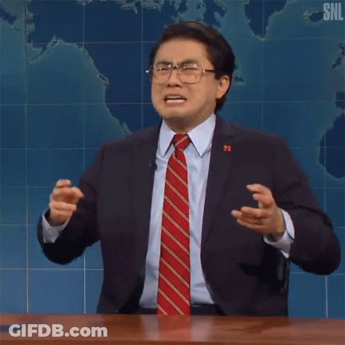 A Man In A Suit And Tie Is Making A Funny Face While Sitting At A Table . GIF