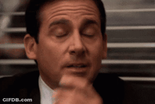 A Man In A Suit And Tie Is Making A Funny Face While Sitting At A Table With His Eyes Closed . GIF