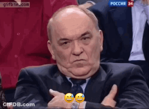 A Man In A Suit And Tie Is Making A Funny Face While Sitting In A Audience . GIF