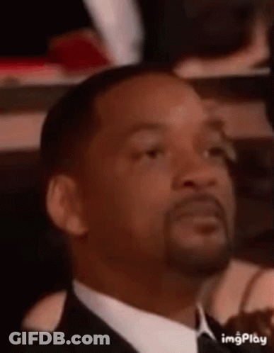 A Man In A Suit And Tie Is Making A Funny Face While Sitting In A Theatre . GIF