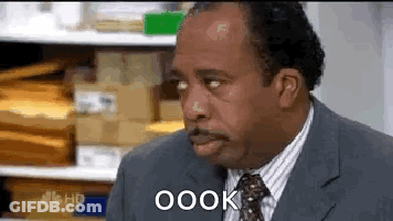 A Man In A Suit And Tie Is Making A Funny Face While Sitting In An Office . GIF