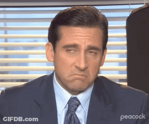A Man In A Suit And Tie Is Making A Funny Face While Sitting In Front Of A Window . GIF