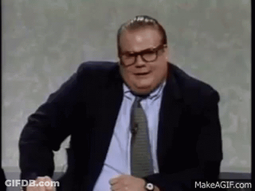 A Man In A Suit And Tie Is Making A Funny Face While Sitting On A Chair . GIF