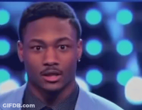 A Man In A Suit And Tie Is Making A Funny Face While Standing In Front Of A Blue Background . GIF