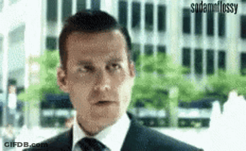 A Man In A Suit And Tie Is Making A Funny Face While Standing In Front Of A Building . GIF