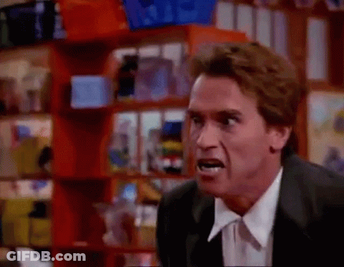 A Man In A Suit And Tie Is Making A Funny Face While Standing In Front Of A Shelf . GIF