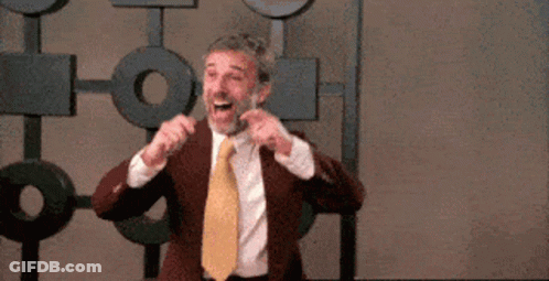 A Man In A Suit And Tie Is Making A Funny Face While Standing In Front Of A Wall . GIF