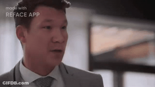 A Man In A Suit And Tie Is Making A Funny Face While Standing In Front Of A Window . GIF