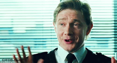 A Man In A Suit And Tie Is Making A Funny Face While Standing In Front Of A Window With Blinds . GIF