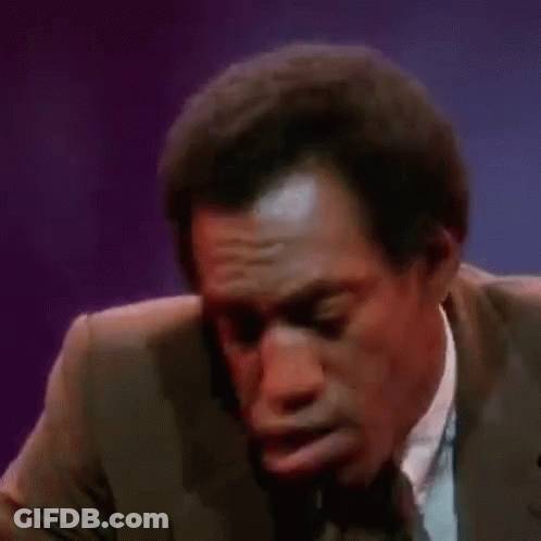 A Man In A Suit And Tie Is Making A Funny Face While Talking Into A Microphone . GIF