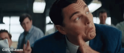 A Man In A Suit And Tie Is Making A Funny Face With His Finger On His Chin GIF